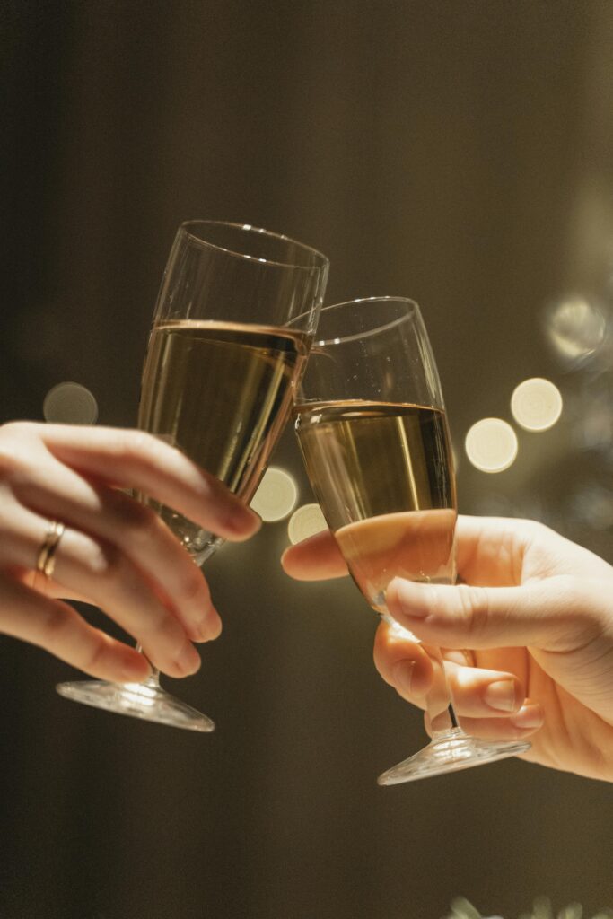 Close-up of hands clinking champagne glasses in a celebratory toast, with elegant bokeh in the background.