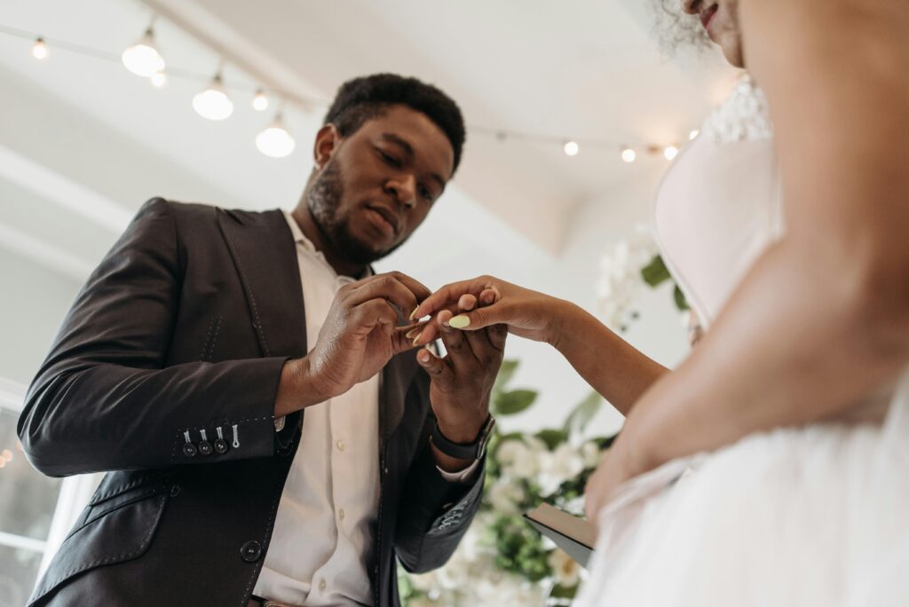 A groom placing a wedding ring on the bride's finger during a romantic indoor ceremony.